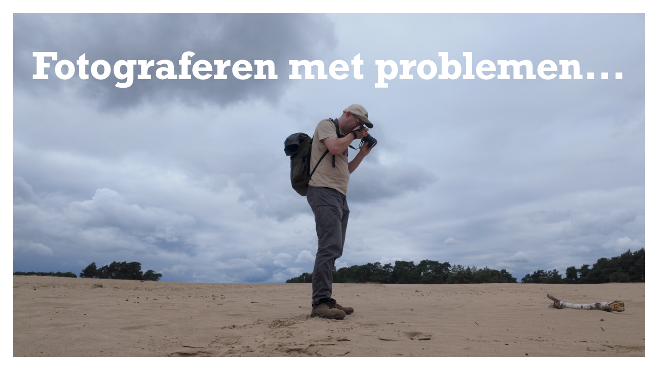Fotograaf staat op het zand in het Wekeromse Zand, richt zijn camera naar beneden en kijkt door de lens naar een stuk hout.